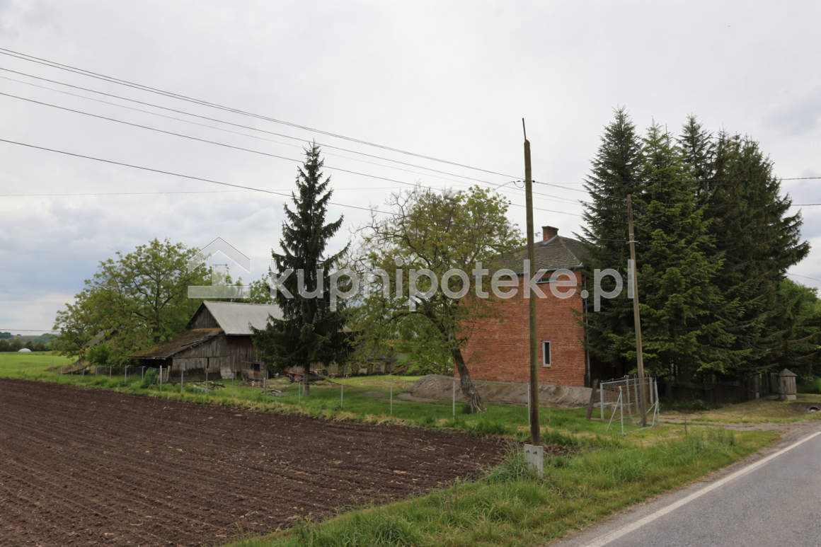 Dom z czerwonej cegły przy drodze, działka z zabudowaniami gospodarczymi i polem, sprzedaż wierzytelności